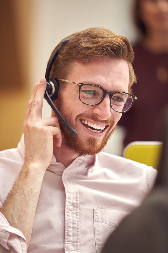 Smiling redheaded man talking into a headset.