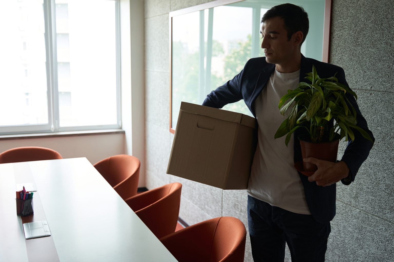 Fired worker carrying box with belongings and plant Laid off employee leaving office with box of possessions in hand and pot with plant
