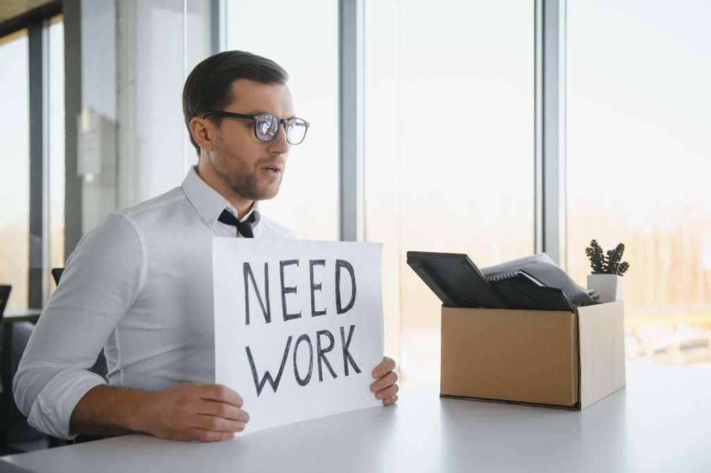 Man sitting with a need work poster