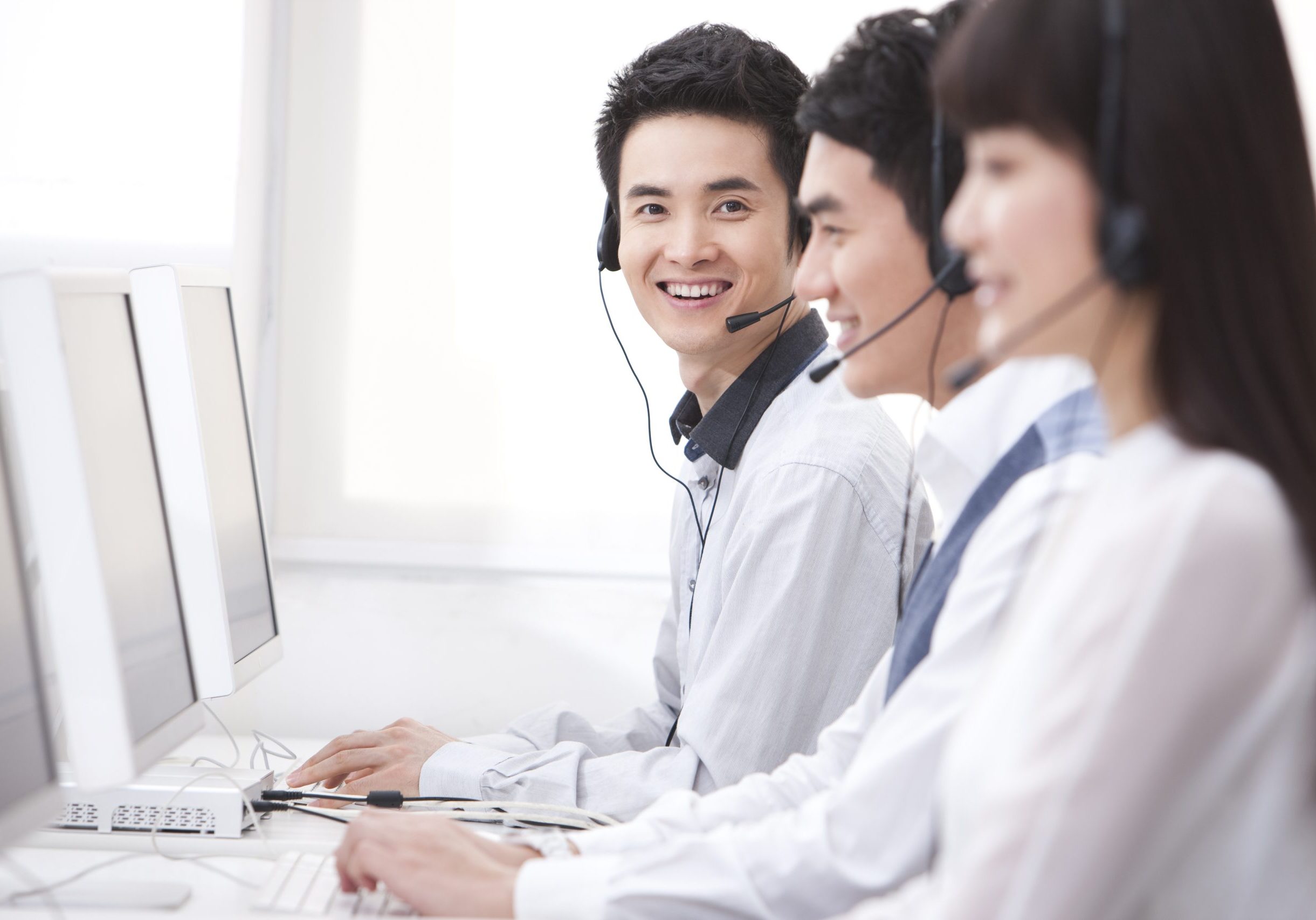 Professional Chinese customer service staff in office Line of people on phone last one smiling